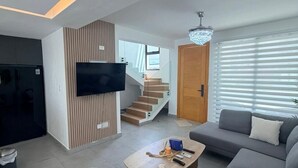 Un soggiorno moderno con una TV a schermo piatto, un divano, un tavolino da caffè e una scala che conduce a un altro piano.