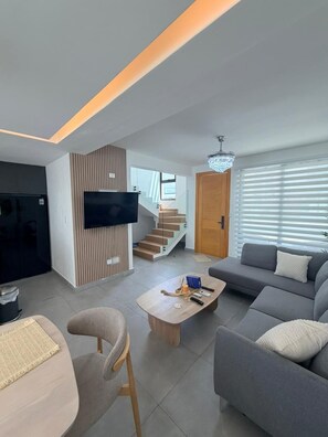 Ein modernes Wohnzimmer mit Flachbildfernseher, Sofa, Couchtisch und einer Treppe, die zu einer anderen Ebene führt.