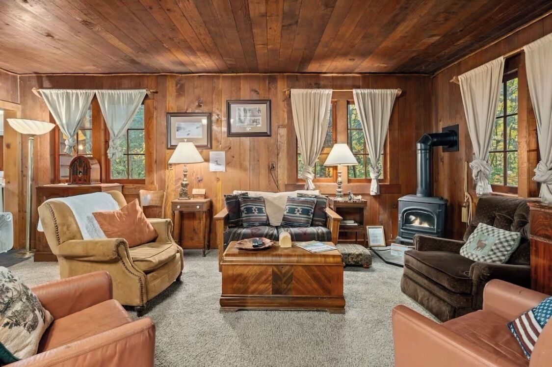 A cozy cabin interior with wooden walls, a fireplace, a sofa, a coffee table, and a lamp.