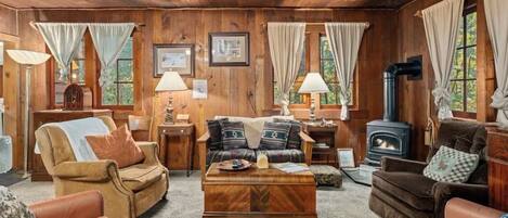A cozy cabin interior with wooden walls, a fireplace, a sofa, a coffee table, and a lamp.