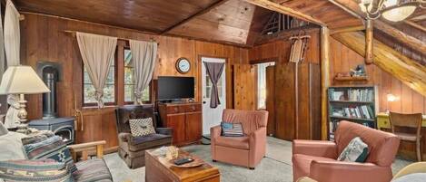 A rustic wooden interior with a fireplace, leather sofas, a television, and a bookshelf.