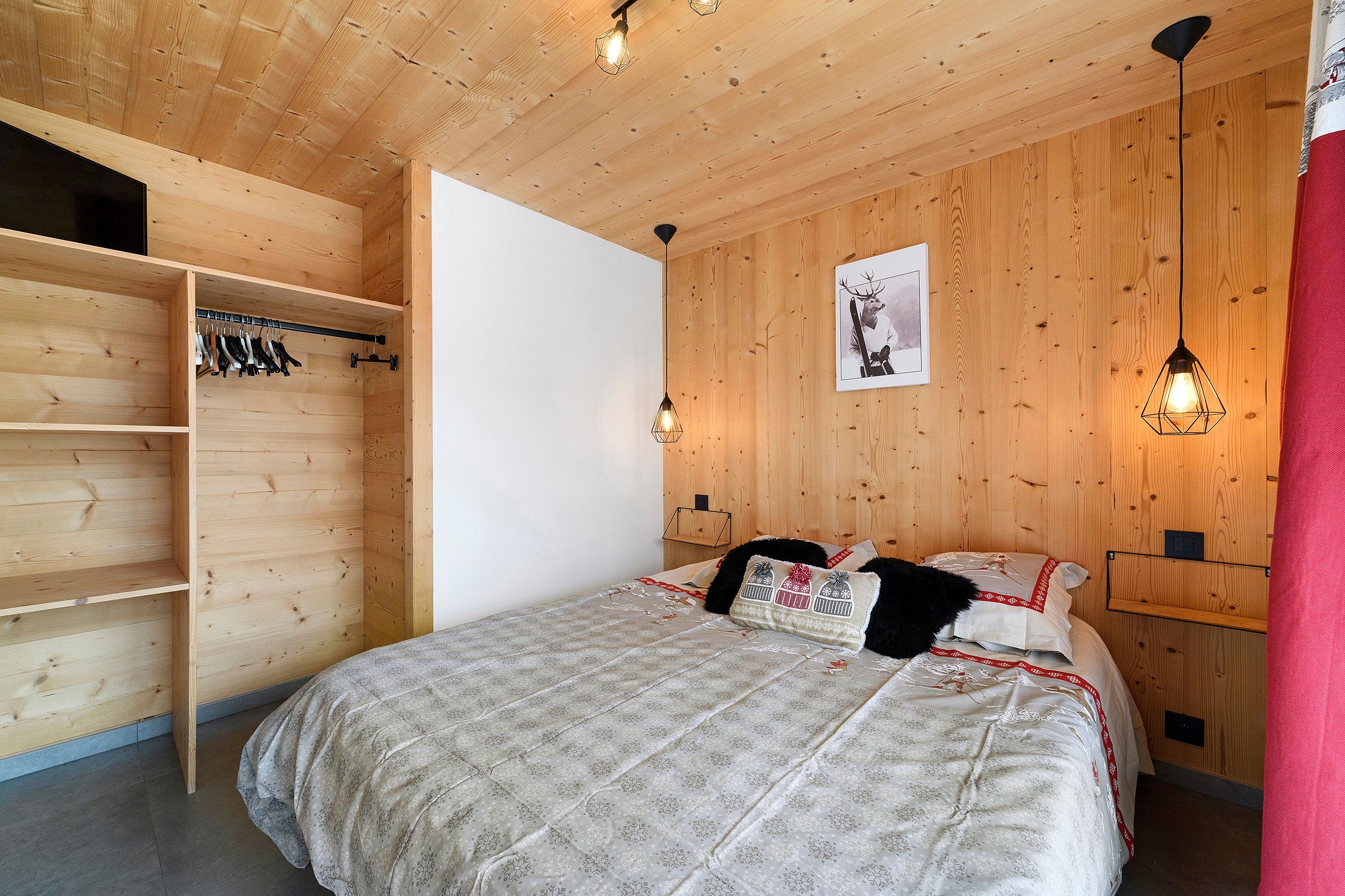 Ein Schlafzimmer mit Holzboden, einem Bett mit gemusterten Betttextilien, einem Kleiderschrank und einer Wandleuchte.