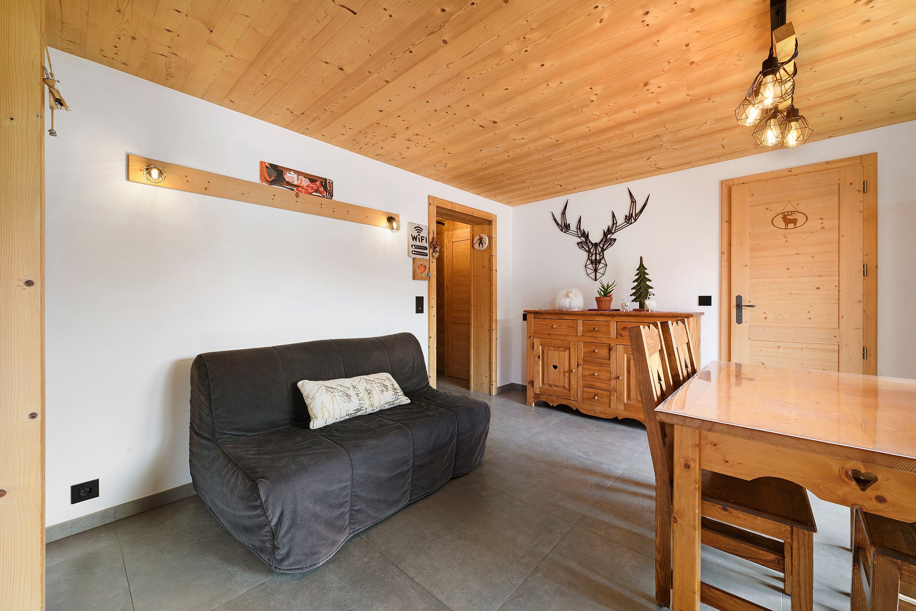 Ein gemütliches Zimmer mit einem dunkelgrauen Sofa, einem Holzschrank und einem Esstisch.