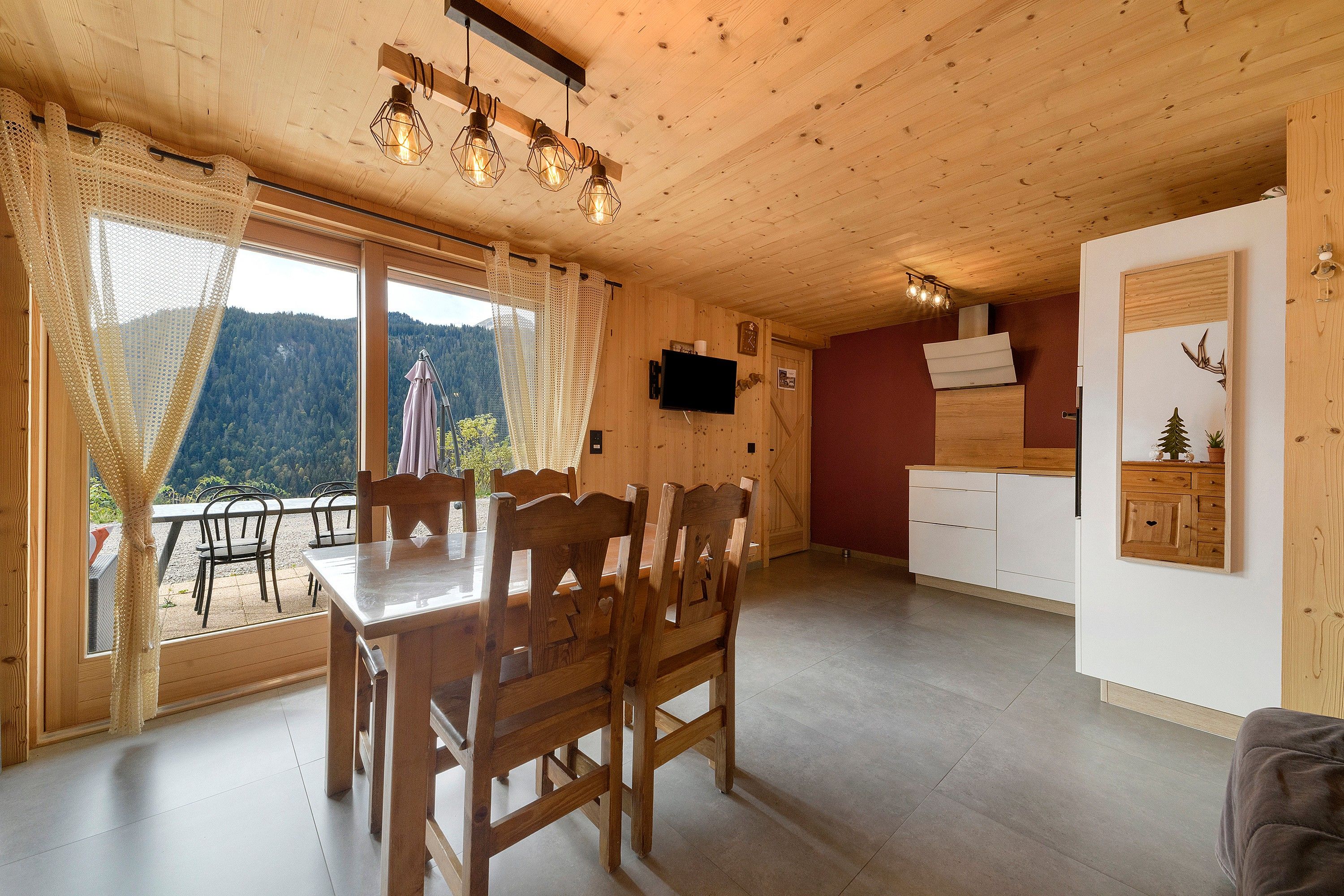 Een houten interieur met een eethoek, keuken en grote ramen met uitzicht op een bebost landschap.