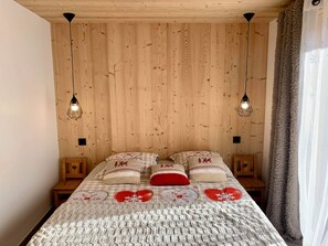 A bedroom with a wooden headboard, a checkered bedspread with heart patterns, and two bedside tables with lamps. - Holiday Home 'New in Detached Chalet' with Private Terrace and Wi-Fi (Châtel)