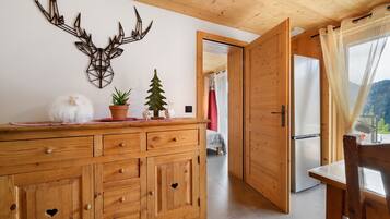 A wooden interior with a cabinet, a decorative wall piece, a small potted plant, and a view through an open door.