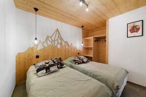 A bedroom with two beds, wooden headboard, pendant lights, a wooden wardrobe, and a framed picture on the wall. - Holiday Home 'New in Detached Chalet' with Private Terrace and Wi-Fi (Châtel)