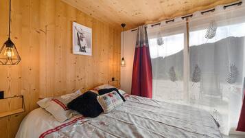 A wooden-paneled room with a bed, a framed picture on the wall, and a window with sheer curtains.