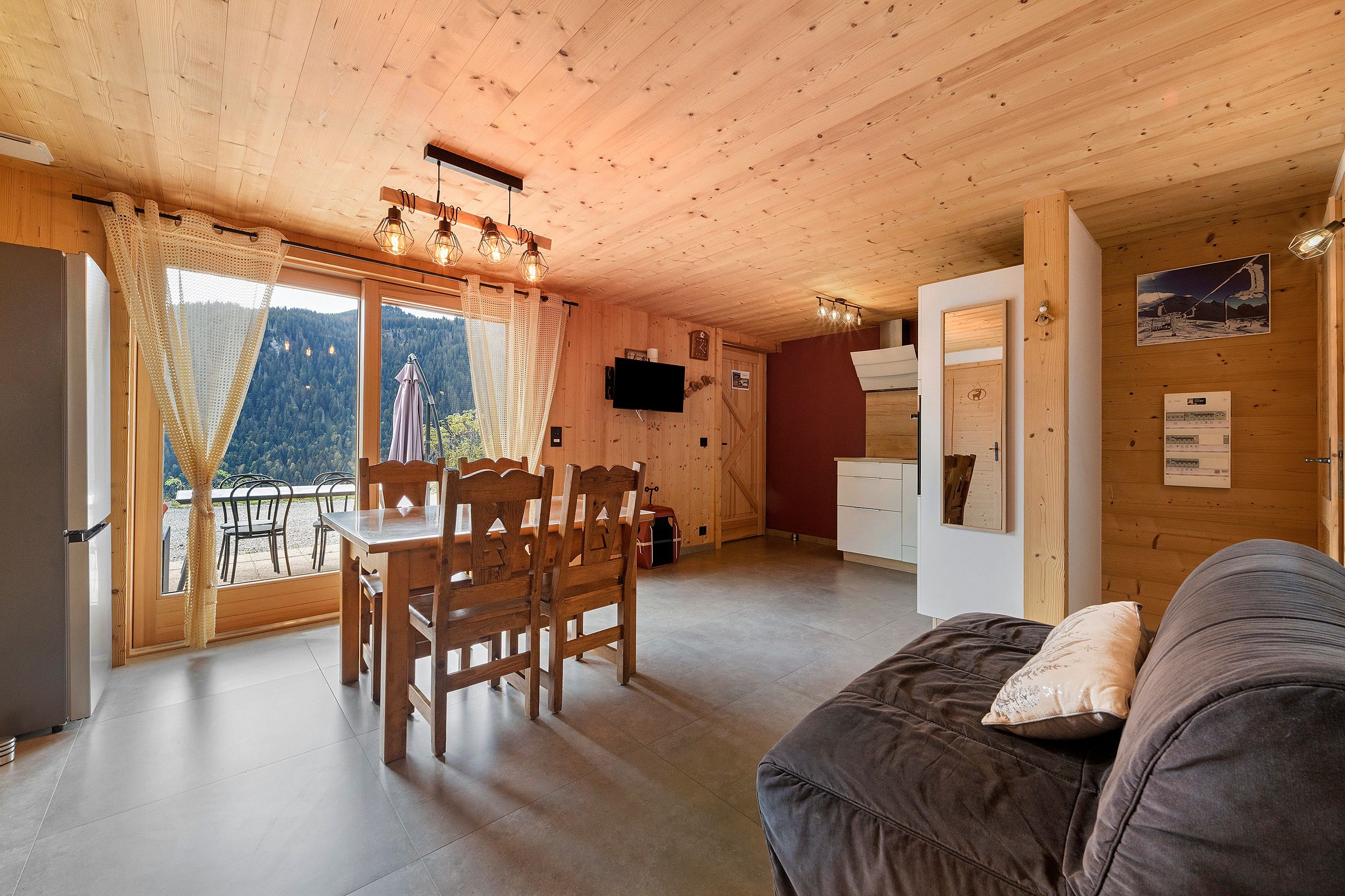 A wooden interior with a dining area, a sofa, and a view through the window.