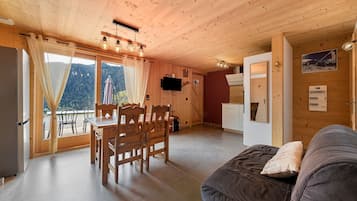 A wooden interior with a dining area, a sofa, and a view through the window.