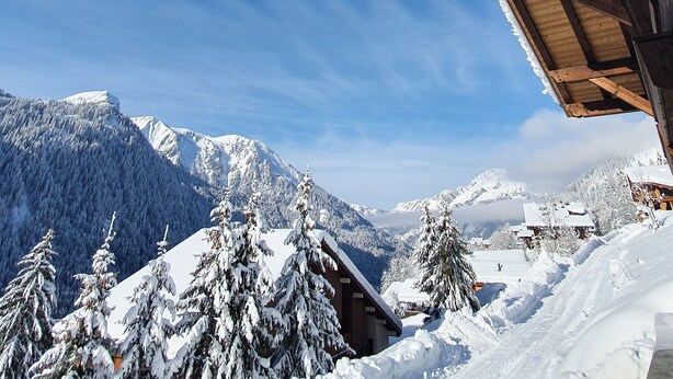 Eine Holzhütte mit geneigtem Dach, umgeben von schneebedeckten Bäumen und Bergen.
