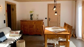 Ein gemütlicher Raum mit Holzbalkendecke, einem Esstisch mit Stühlen, einer Couch mit Zierkissen und einem Schrank mit Blumen in einer Vase.