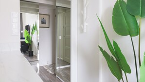 A modern interior with a glass door leading to a room, a potted plant, and a white wall with a picture frame. - Stylish Studio in the Heart of Kallio (Helsinki)