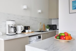 A modern kitchen with a coffee maker, sink, dishwasher, and a bowl of fruit on the counter. - Stylish Studio in the Heart of Kallio (Helsinki)