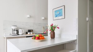 A modern kitchen with a marble backsplash, a coffee maker, a fruit bowl, and a vase with flowers. - Stylish Studio in the Heart of Kallio (Helsinki)