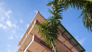 Un immeuble à plusieurs étages doté de balcons, d’un escalier central et d’un palmier.