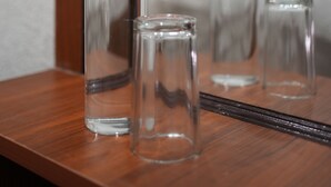 Une étagère en bois sur laquelle reposent trois bouteilles en verre transparent, et un miroir qui reflète un lit et un mur.
