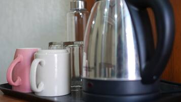 A kitchen area with a kettle, a pink mug, and a white mug on a tray.