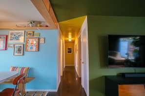 A hallway with a dining area, artwork on the walls, a television, and a staircase.