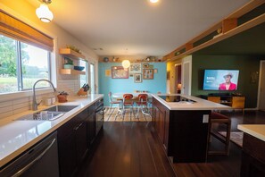 A modern kitchen with a central island, a dining area with chairs, and a television on the wall.