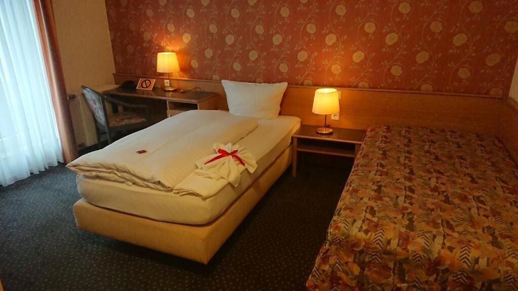 A hotel room with a bed, a desk, two lamps, a chair, and a nightstand.