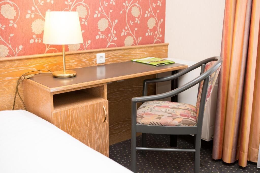 Een hotelkamer met een houten bureau, een stoel, een lamp en een bed.