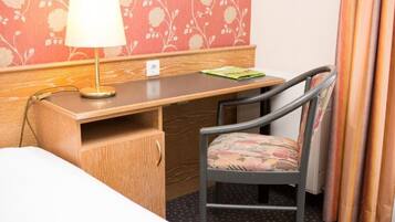 Een hotelkamer met een houten bureau, een stoel, een lamp en een bed.