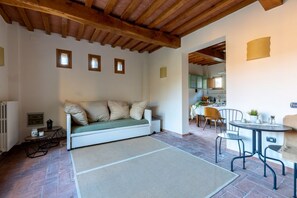 A cozy room with a sofa, a dining table with chairs, a radiator, and a kitchen visible through an open doorway. - GuestHost - Charming apartment located inside an old renovated barn in an agricultural estate on the Tuscan hills, surrounded by nature and with a breathtaking view of the surrounding countryside. The property, equipped with private outdoor parking, outd (Palaia)