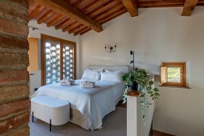A bedroom with a large bed, a bench, a potted plant, and a window with a view. - GuestHost - Charming apartment located inside an old renovated barn in an agricultural estate on the Tuscan hills, surrounded by nature and with a breathtaking view of the surrounding countryside. The property, equipped with private outdoor parking, outd (Palaia)