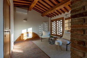 Une pièce avec un sol en briques, des poutres en bois au plafond, un canapé blanc, une petite table ronde et une fenêtre ornée d’un motif en treillis.