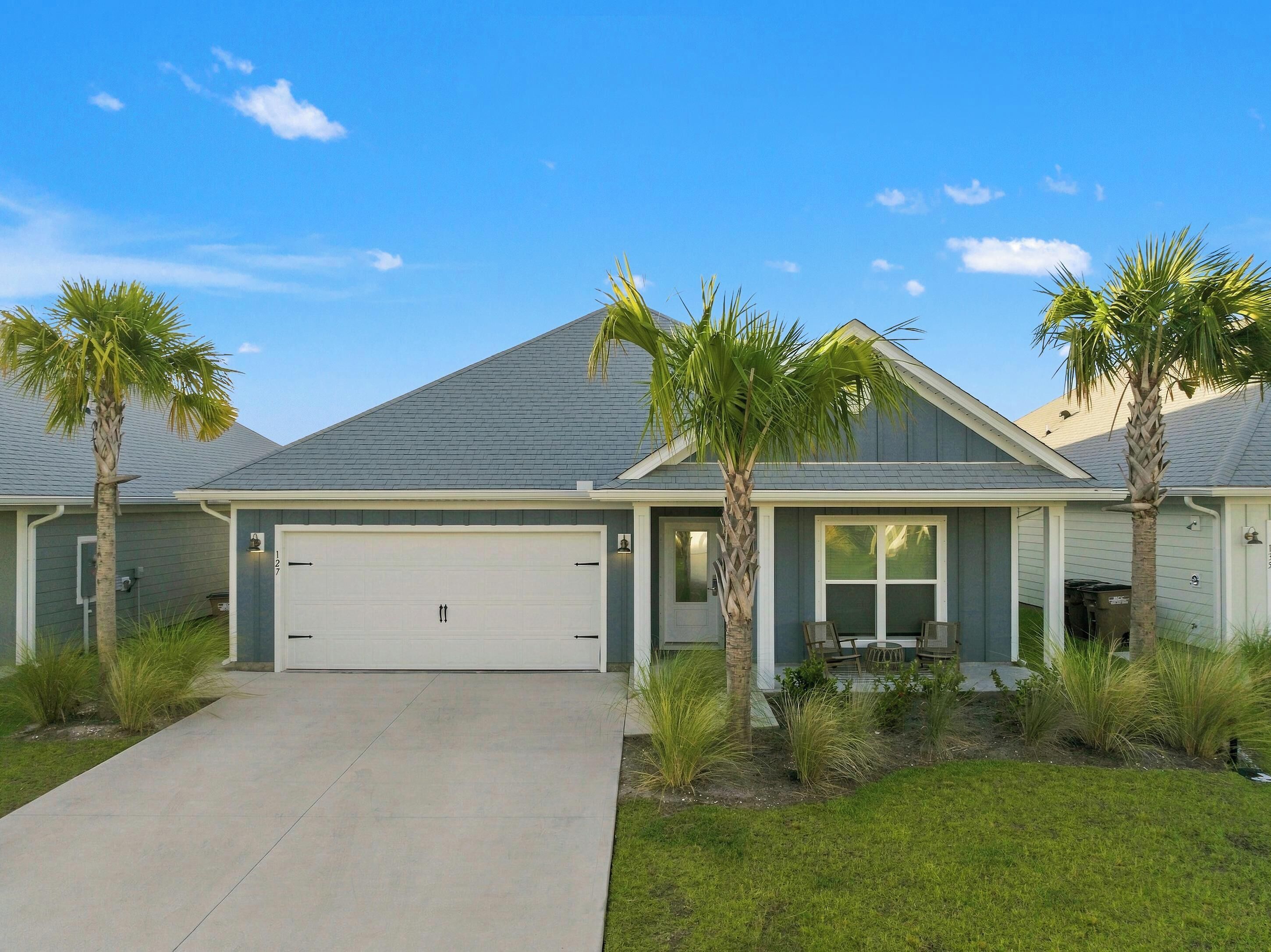 A residential house with a garage, two palm trees, and a well-maintained lawn.