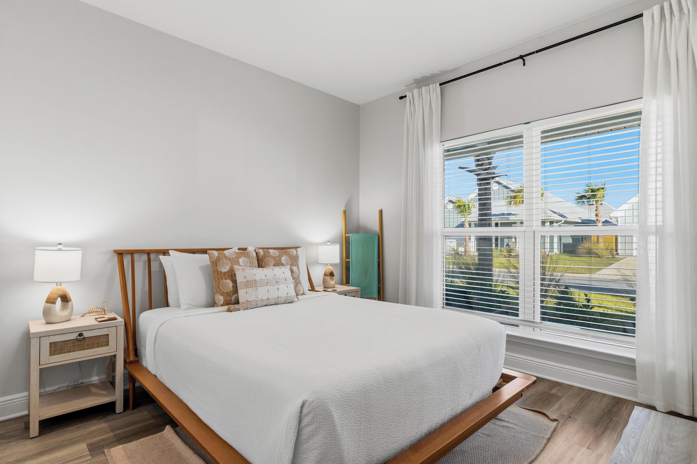 A modern bedroom with a large bed, bedside tables, a view of the outside, and a window with blinds.
