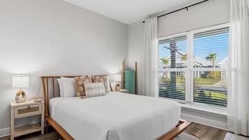 A modern bedroom with a large bed, bedside tables, a view of the outside, and a window with blinds.