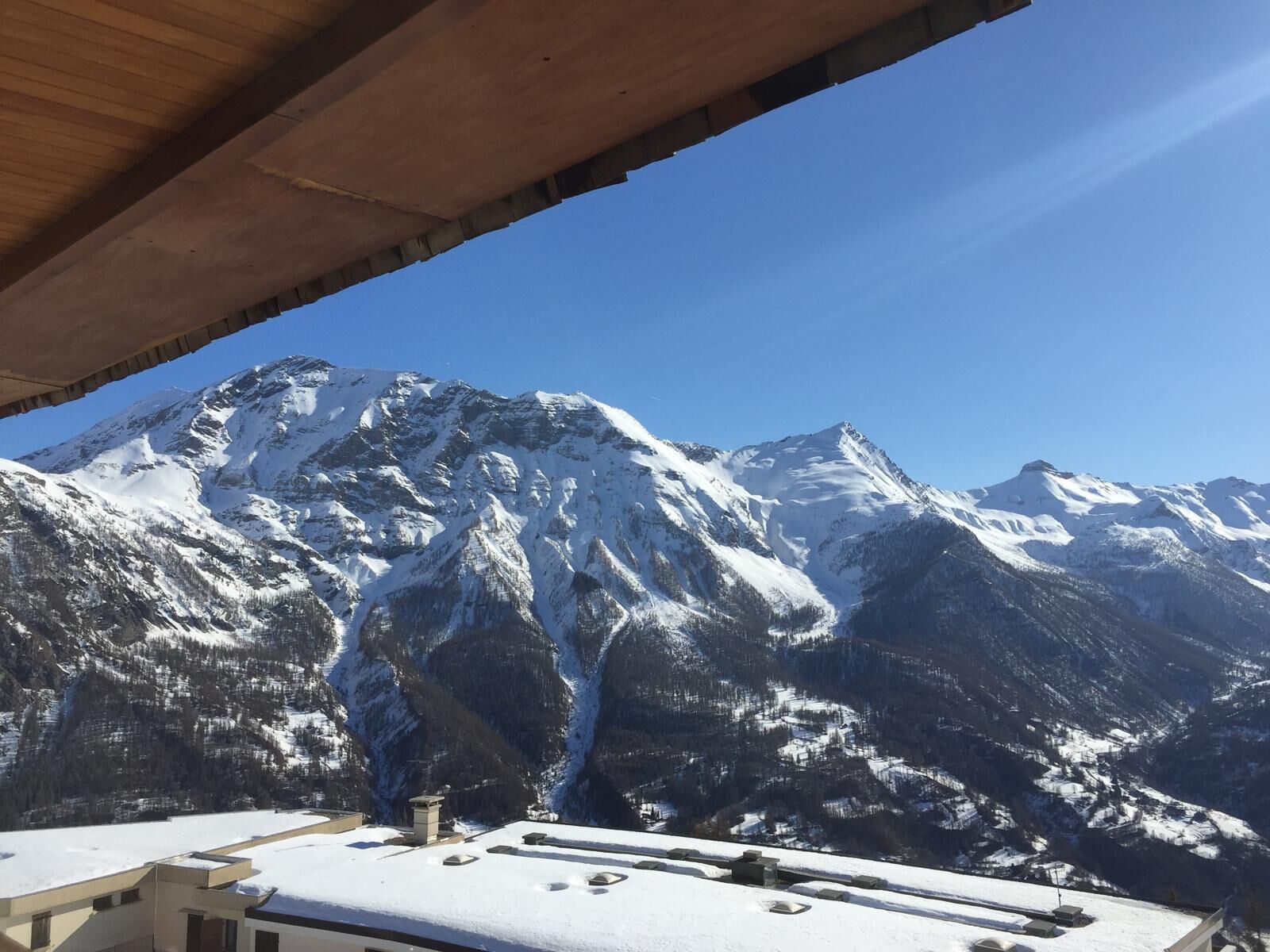 Blick auf Berge von einer überdachten Außenbereits mit schneebedeckten Gipfeln und blauem Himmel.