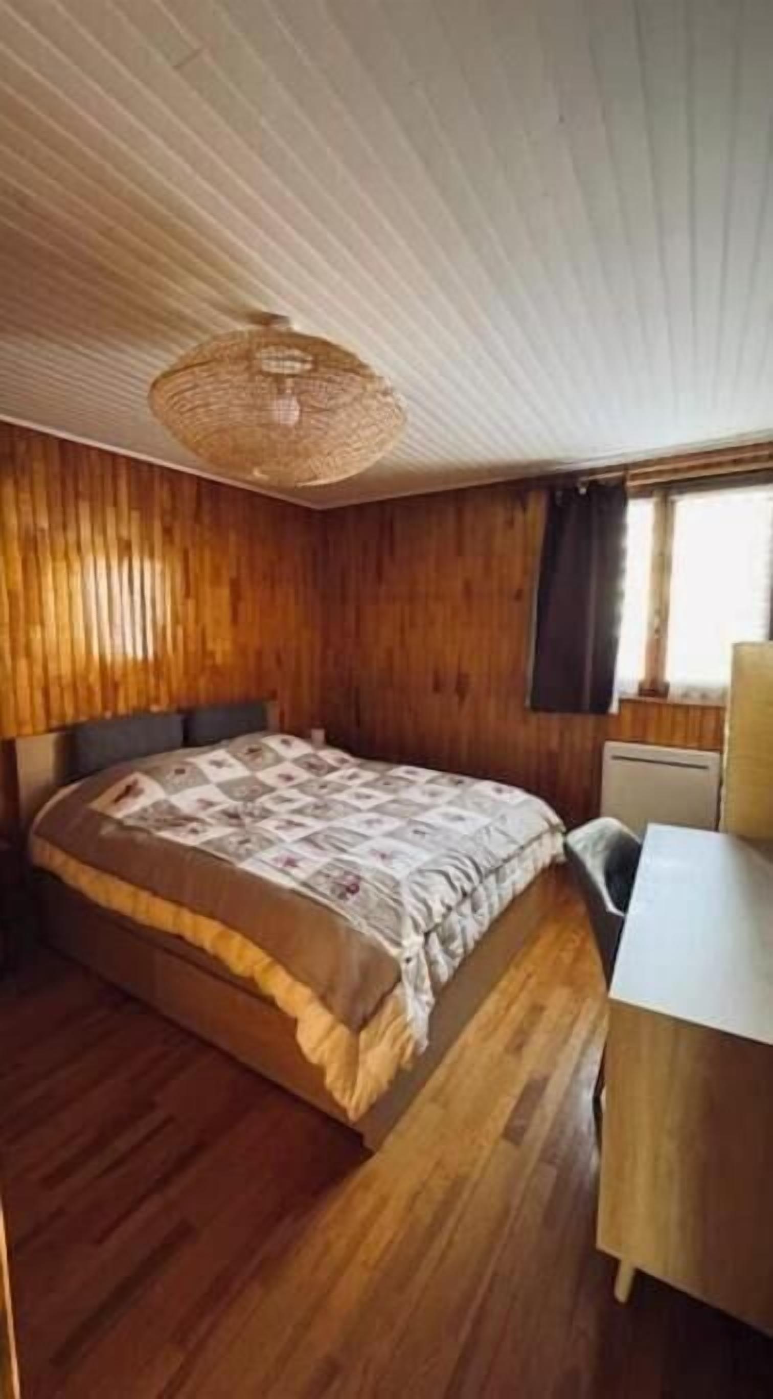 A bedroom with a bed, a desk, and a window.