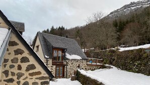 A stone house with a sloped roof, a wooden balcony, and a stone wall with snow. - Charming Small Cottage for 2/3 Guests – La Chèvrerie (Saint-Vincent-de-Salers)