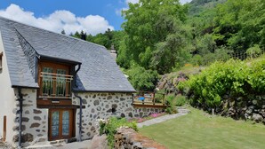 A stone house with a sloped roof, a wooden door, and a small balcony. - Charming Small Cottage for 2/3 Guests – La Chèvrerie (Saint-Vincent-de-Salers)