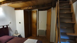 A bedroom with a bed, a nightstand, a vase, and a wooden staircase. - Charming Small Cottage for 2/3 Guests – La Chèvrerie (Saint-Vincent-de-Salers)