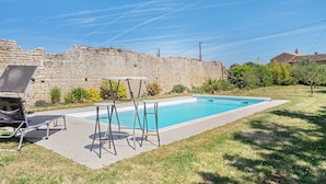 Ein Schwimmbad mit Steinwand im Hintergrund, Sitzgelegenheiten im Freien und blauem Himmel.