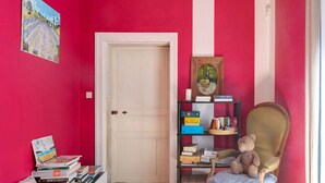 Ein Zimmer mit roter Wand, weißer Tür, Bücherregal, Stuhl und kleinem Tisch.