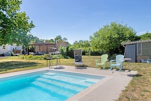 A swimming pool with lounge chairs and a table, surrounded by a grassy area and trees.