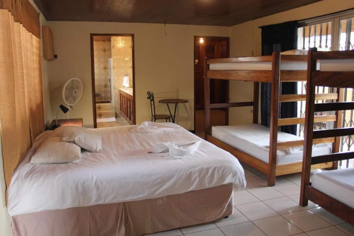 Une pièce comprenant un lit, des lits superposés, un ventilateur, une petite table et une fenêtre.