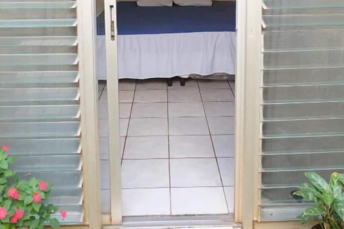 Une chambre avec un lit, un luminaire au plafond et une porte-fenêtre coulissante donnant sur un balcon.