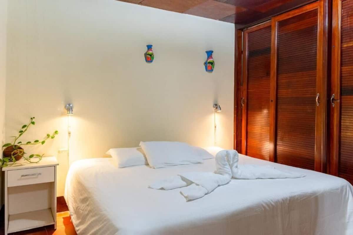 Une chambre d’hôtel comprenant un lit, une table de chevet, des lampes fixées au mur et une armoire.