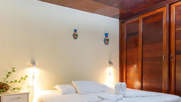 Ein ordentlich bezogenes Bett mit weißen Leinen, ein Nachttisch mit Lampe und ein Holzschrank.
