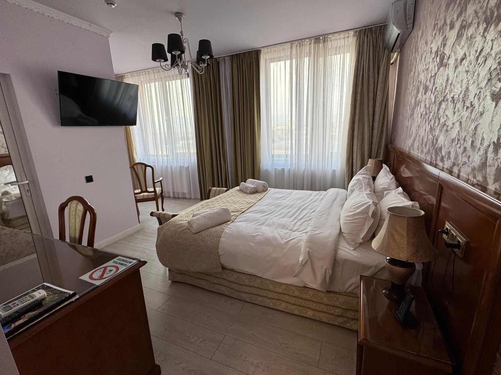 A hotel room with a bed, a desk, a chair, a television, and a window with curtains.
