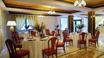 A dining area with round tables, red chairs, chandeliers, and a large decorative rug.