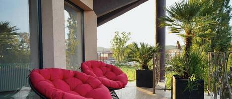 Een balkon met twee rode stoelen en pottenplanten.