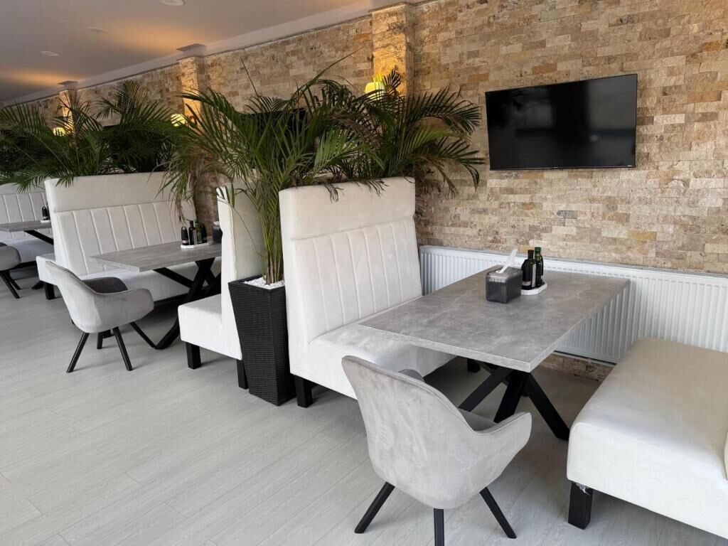 A modern lounge area with white cushioned seating, a flat-screen TV mounted on a brick wall, and a potted plant.