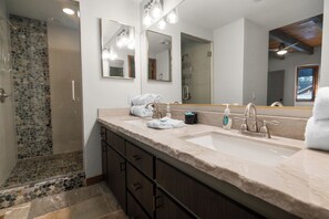 A bathroom with a double sink, a large mirror, and a shower area with a pebble wall. - Evergreen (Big Bear Lake)